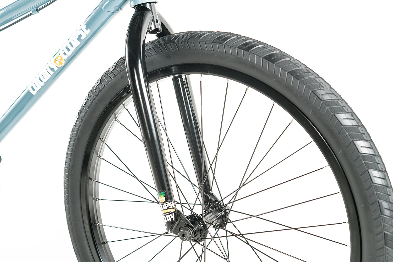 Close-up of the front wheel and black fork, highlighting tire tread, spokes, and part of the blue chromoly frame on the Colony Eclipse 24 Inch Bike against a white background.