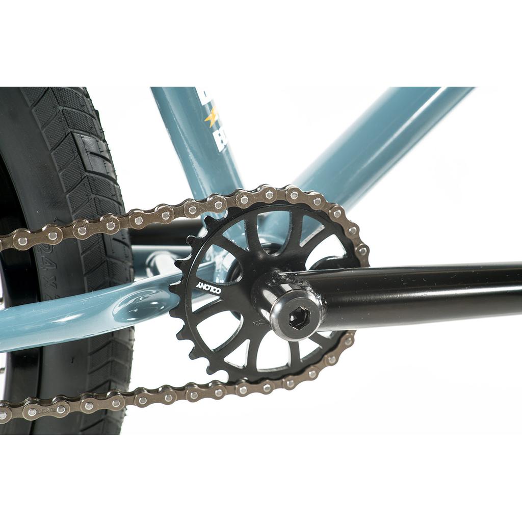 Close-up view of the bicycle chain, chainring, and crank arm on the blue chromoly frame of a Colony Eclipse 24 Inch Bike with a black rear tire.