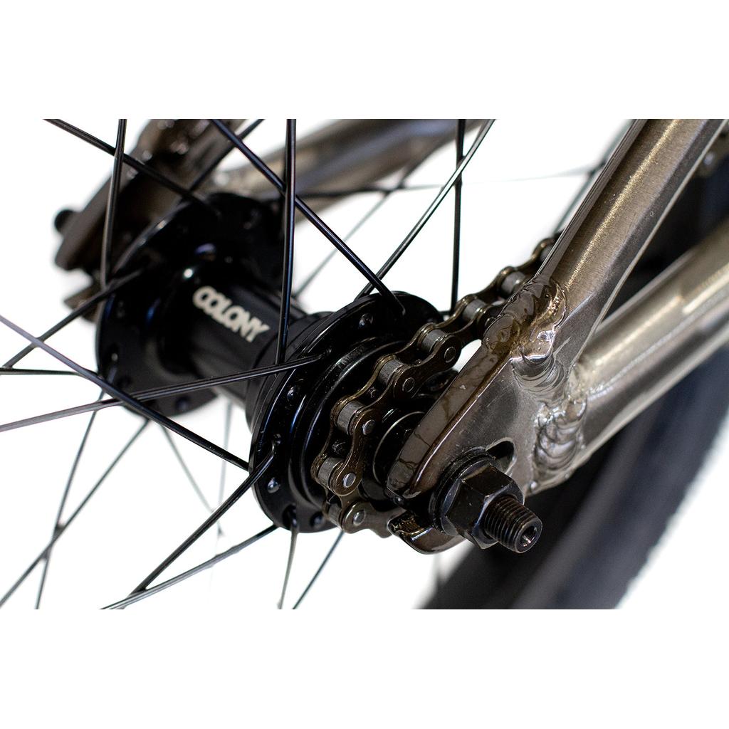 Close-up of the Colony Horizon 16 Inch Bike’s rear wheel hub, displaying black spokes, a metal chain, and axle nuts against a white background.