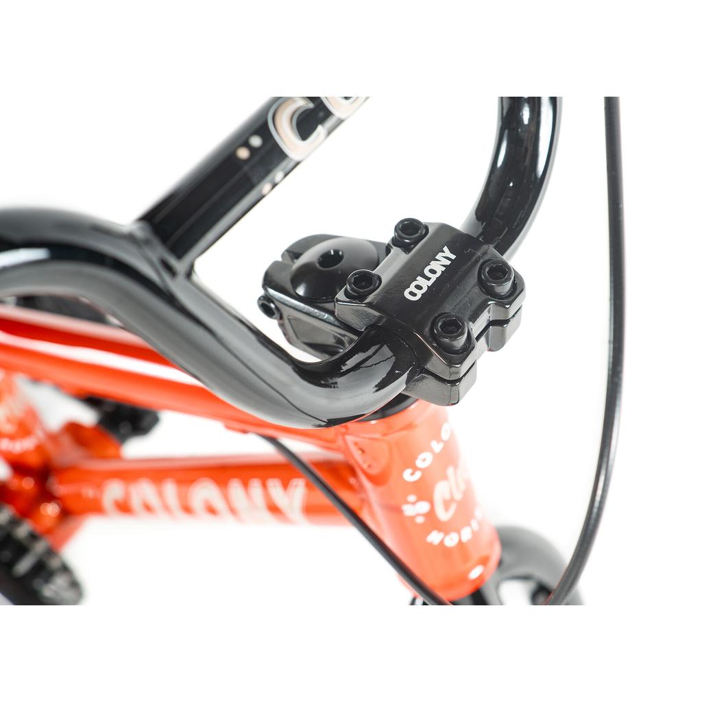 Close-up of the black handlebar and stem on the Colony Horizon 12 Inch Bike, featuring an orange alloy frame and visible cables against a white background.