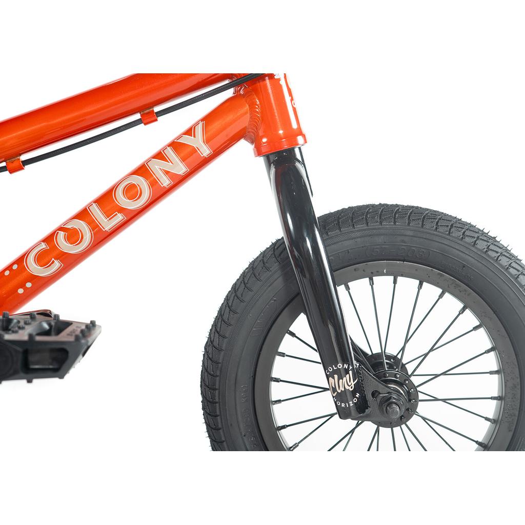 A close-up of the Colony Horizon 12 Inch Bike highlights its red lightweight alloy frame, black fork, black front wheel, and part of the pedal against a white background.