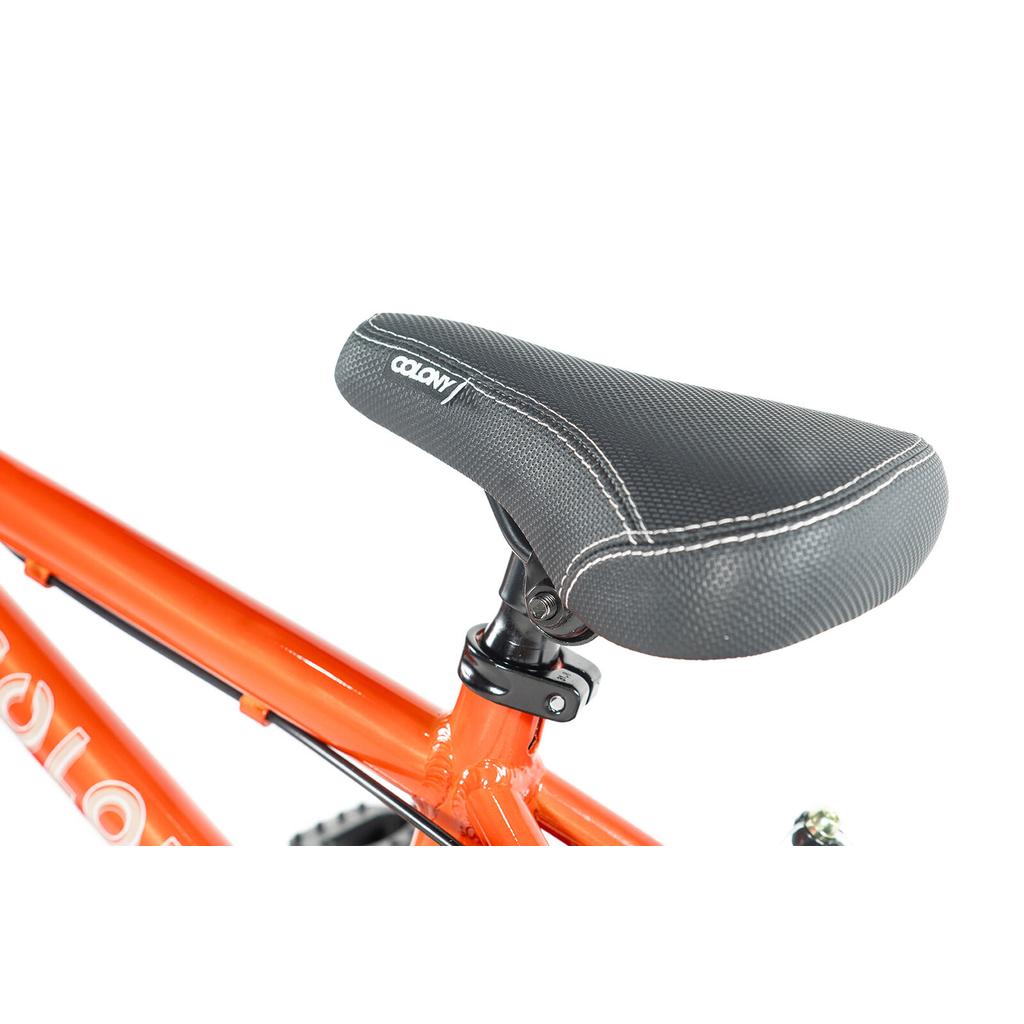 Close-up of a black bicycle seat with white stitching on a lightweight alloy frame, part of the Colony Horizon 12 Inch Bike, with the Colony logo partially visible on the vibrant orange frame.