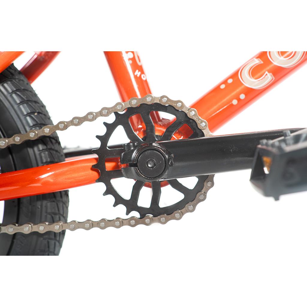 Close-up of a Colony Horizon 14 Inch Bike chain and black sprocket on an orange frame, highlighting the pedal arm and part of the rear tire—ideal for aspiring freestyle athletes.