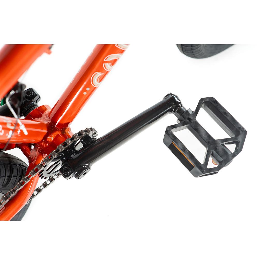 Close-up of a black bicycle pedal and crank arm on the Colony Horizon 20 Inch Bike in orange, featuring part of the chain and rear wheel—perfect for freestyle BMX riders aiming for Olympic-level performance.