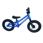 A small blue Colony BMX Horizon Alloy Balance Bike for kids, featuring black tires and handlebars, sits on a green floor against a white wall. Ideal as a first BMX balance bike for young riders.