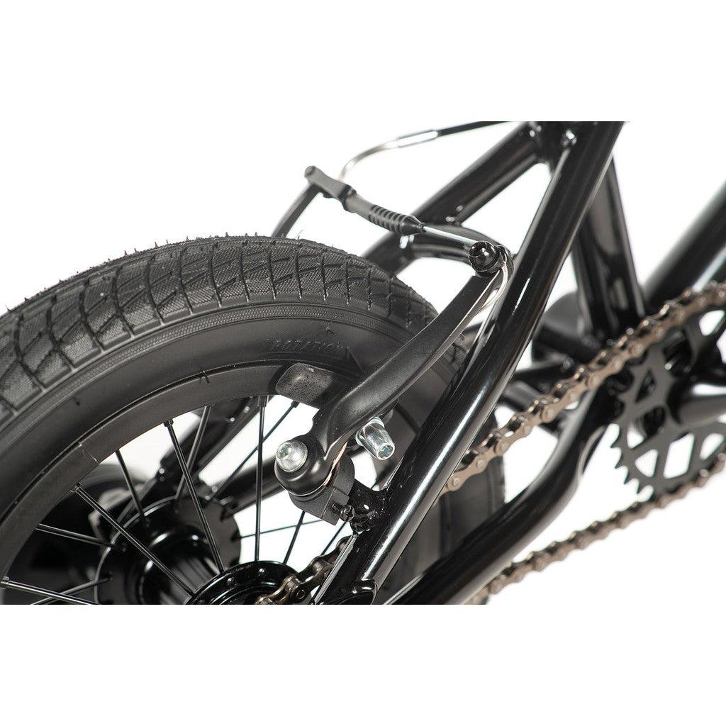 Close-up of the Division Blitzer 12 Inch Bike's rear wheel, highlighting a tire with visible tread, black spokes, a brake caliper, and a chain wrapped around the gears. Ideal for those looking for an entry-level ride that combines style and functionality.