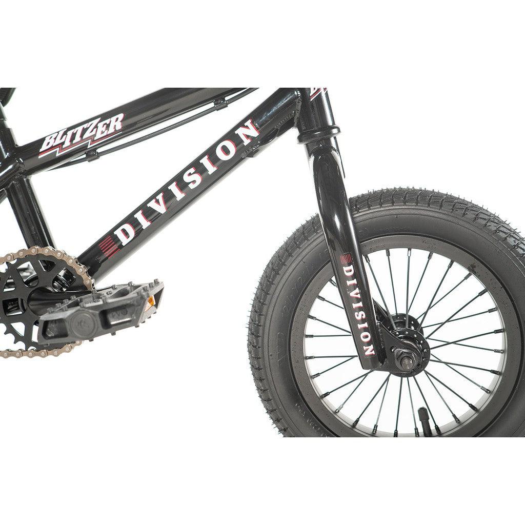 Close-up of a Division Blitzer 12 Inch Bike, highlighting the front wheel, pedal, and portion of the frame with the "Division" branding prominently displayed. Ideal for entry-level riders looking for style and performance.