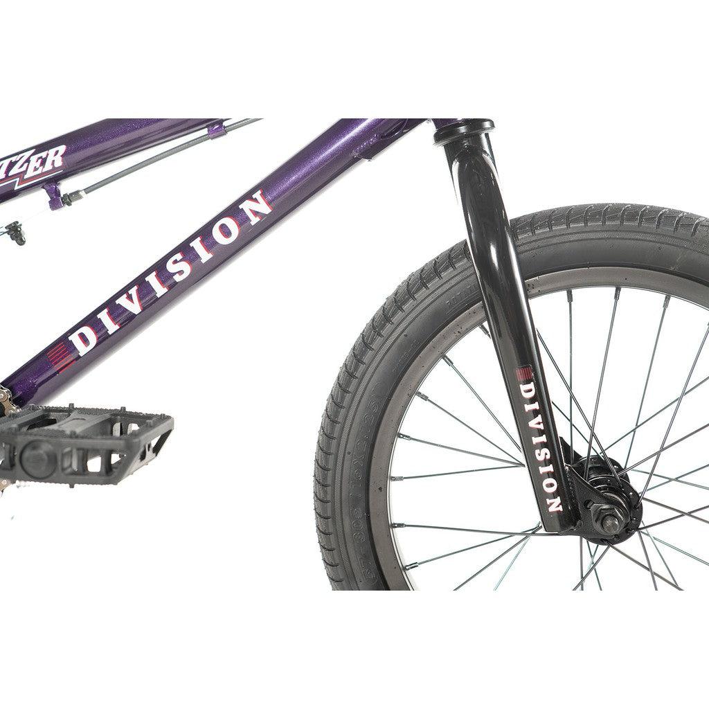 Close-up of the Division Blitzer 16 Inch Bike in purple, showcasing "Division" branding on the frame and fork, equipped with black pedals and a front tire featuring 16-inch tires for an entry-level BMX experience.