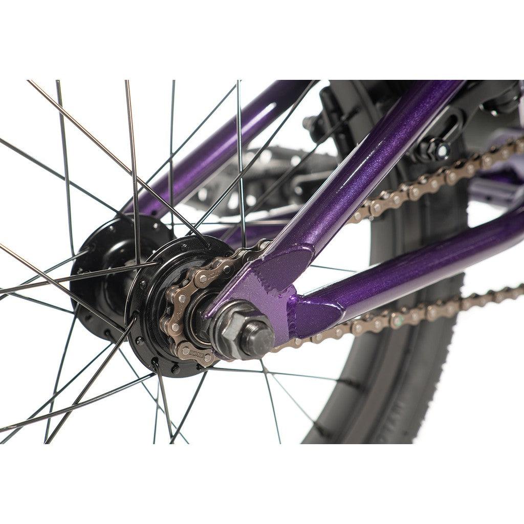 Close-up of the Division Blitzer 16 Inch Bike's rear wheel and chain mechanism, highlighting its metallic purple frame and black tire. This entry-level BMX bike is designed with scaled down geometry for optimal performance and style.