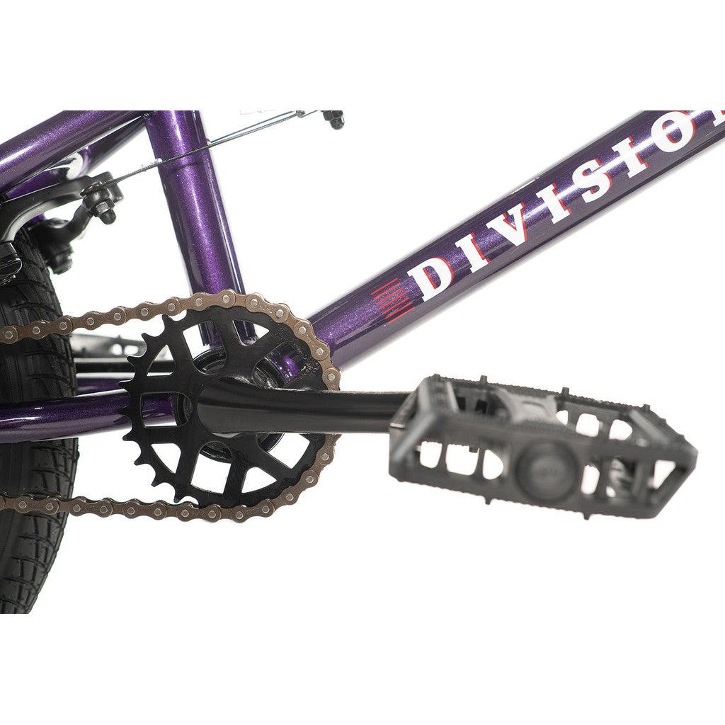 Close-up of the Division Blitzer 16 Inch Bike, featuring a purple frame with scaled-down geometry perfect for an entry-level BMX ride. Highlights include the black pedal, crank, and chainring, along with a peek at the rear tire. The brand name "Division" is prominently displayed on the frame.