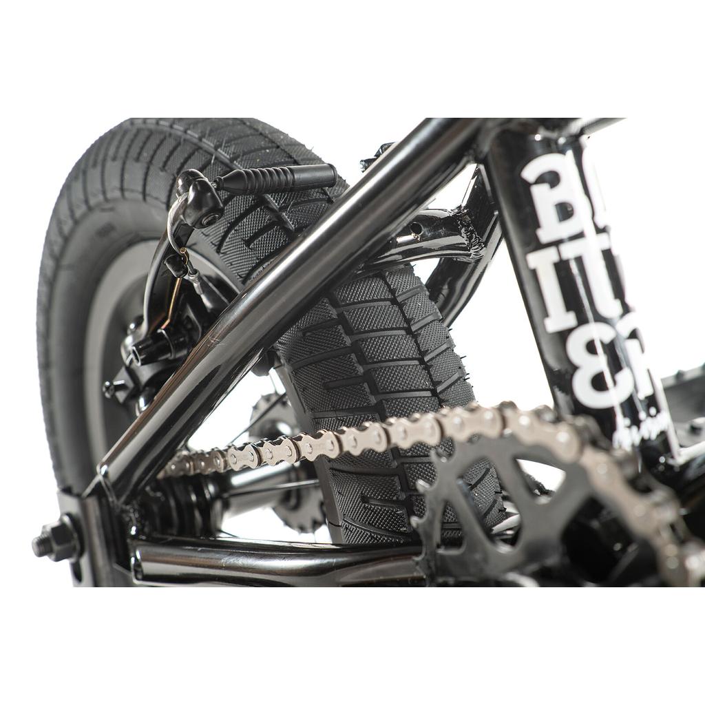 Close-up view of the Division Blitzer 12 Inch Bike’s black rear wheel, tire, chain, and frame, highlighting detailed gear and brake components.