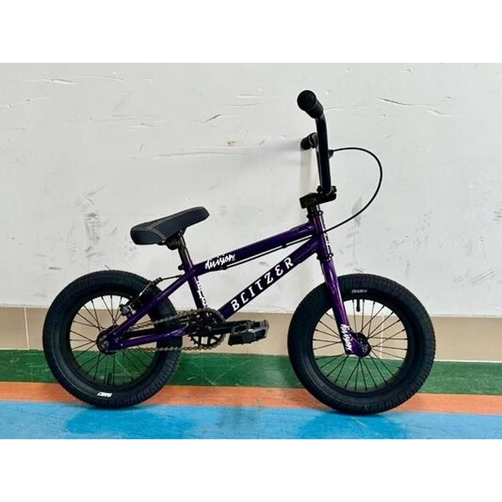 The Division Blitzer 14 Inch Bike, a small purple BMX perfect for young riders, is parked indoors against a white wall with a green and blue floor.