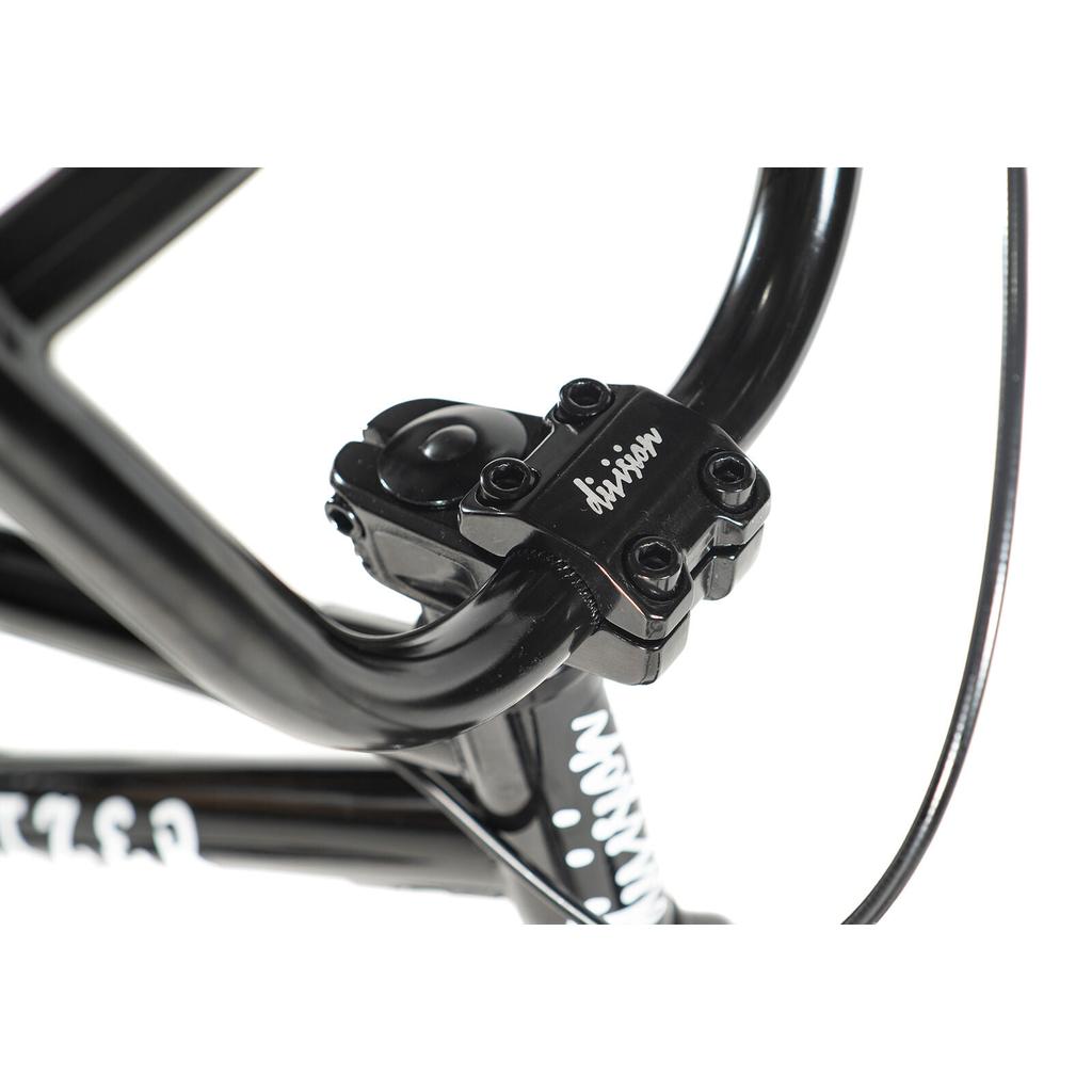 Close-up of the Division Blitzer 16 Inch Bike's black BMX handlebar stem with "division" printed on top, featuring visible bolts and part of the youth bike frame with 16-inch wheels.