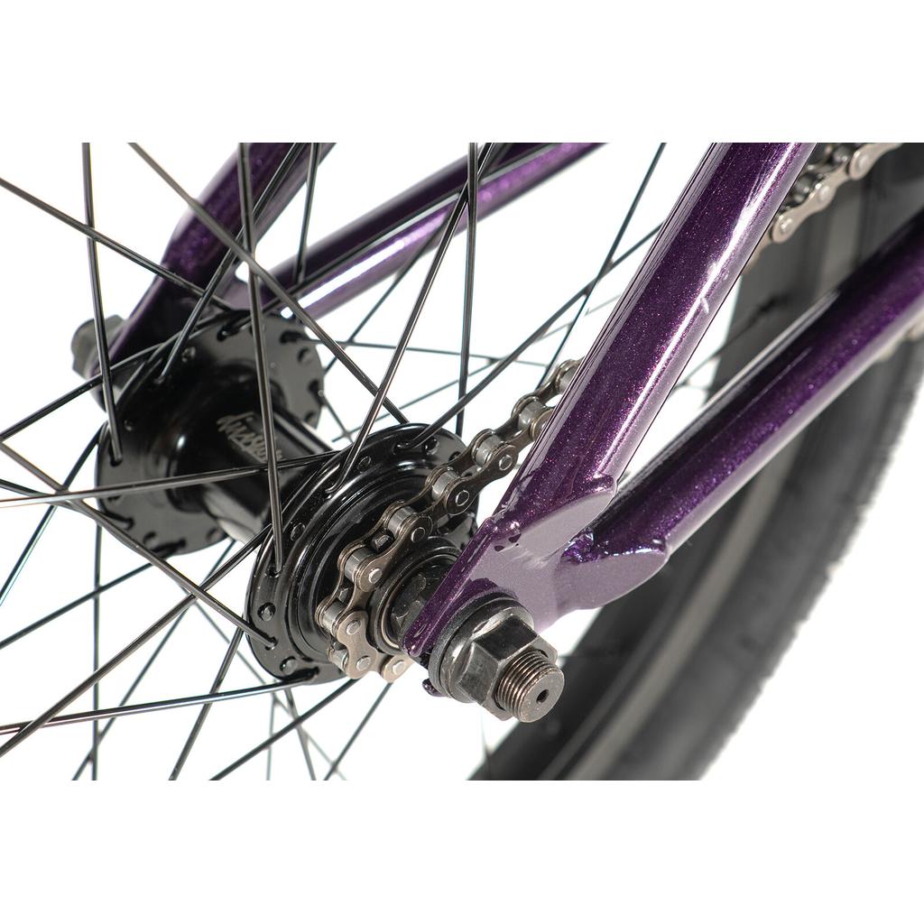 Close-up of the Division Blitzer 18 Inch Bike’s rear wheel, showing the cassette hub, spokes, chain, and part of its metallic purple frame.