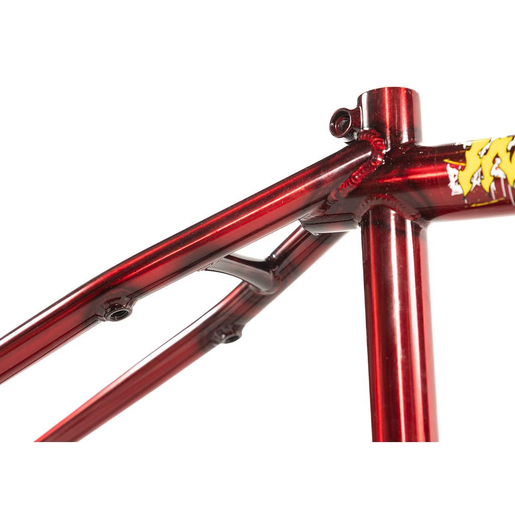 Close-up of the Colony Injustice Frame (Tom Justice Signature) in metallic red, crafted from 4130 CrMo, displaying welded joints and sections of the top tube, seat tube, and seat stay, with a partially visible yellow graphic.