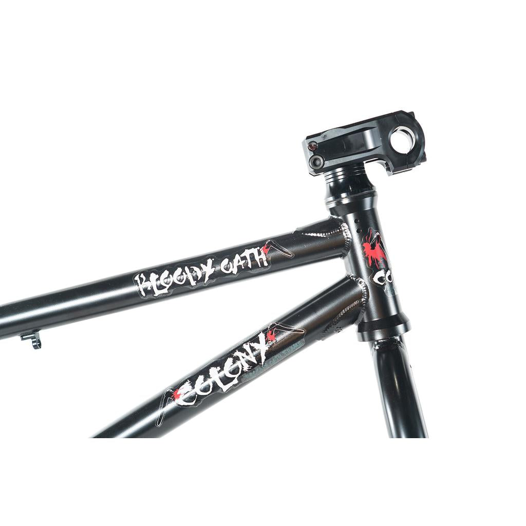 The Colony Bloody Oath Frame Kit, a limited edition BMX frame in matte black with "Bloody Oath" and "Colony" graphics, is pictured with a stem attached to the head tube and stands out against a white background.