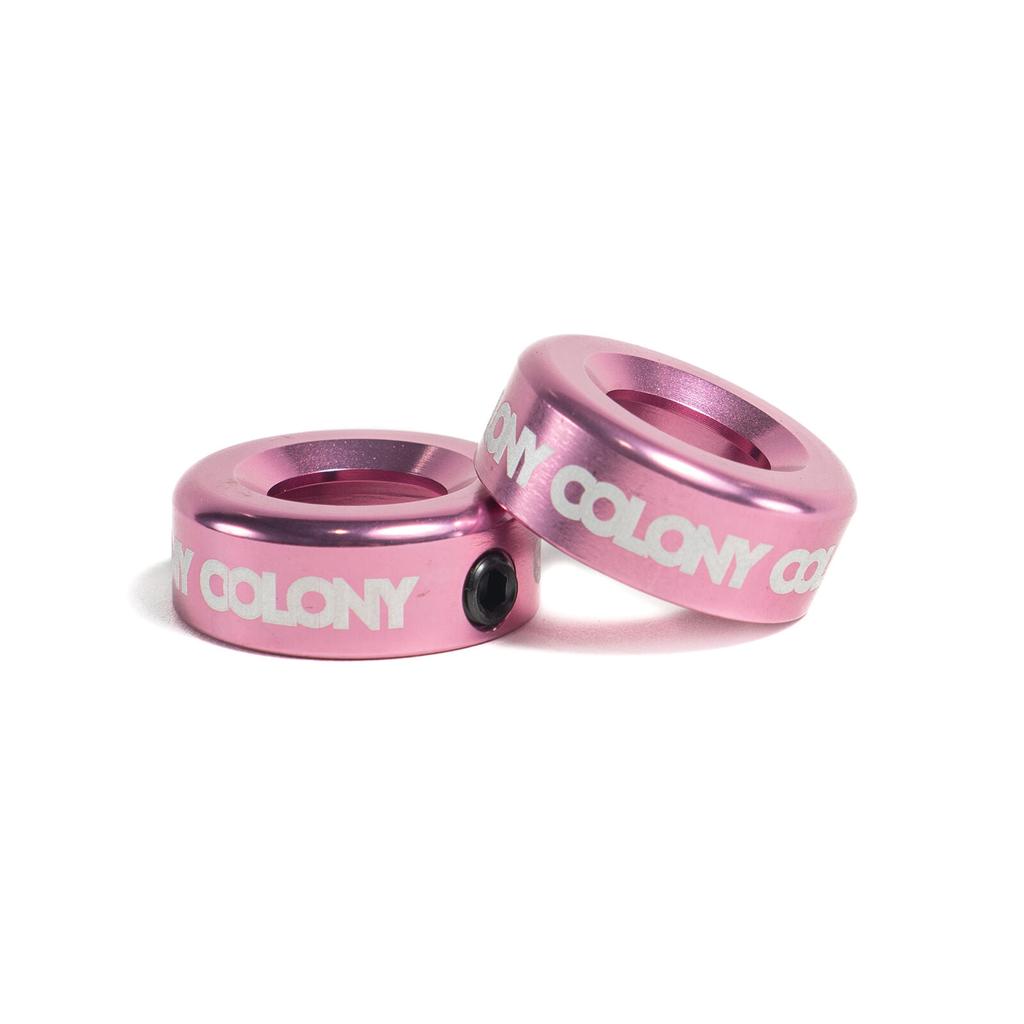 Two pink CNC-machined Colony Konka Bar Ends with white "COLONY" branding are stacked at an angle on a white background—essential BMX accessories for riders who want both durability and style.