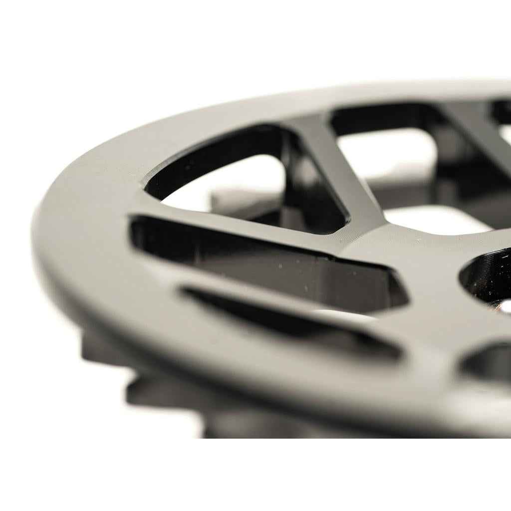 Close-up of a black Colony Bish Guard Sprocket, featuring triangular openings and beveled edges. CNC machined from aluminum, it showcases a lightweight design resembling a gear or mechanical part.