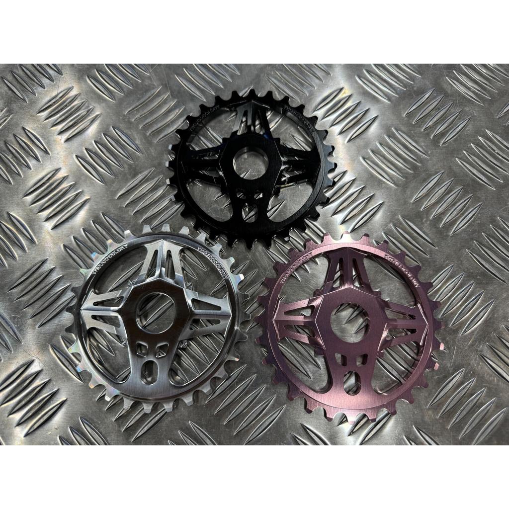Three Colony CC Sprockets, crafted from black, silver, and purple 7075T6 Alloy, are displayed on a diamond plate metal surface.