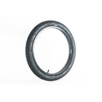 The Family BMX F603 18 Inch Tyre, black and fitted with a valve stem, stands upright against a plain white background, highlighting its versatile tread pattern.