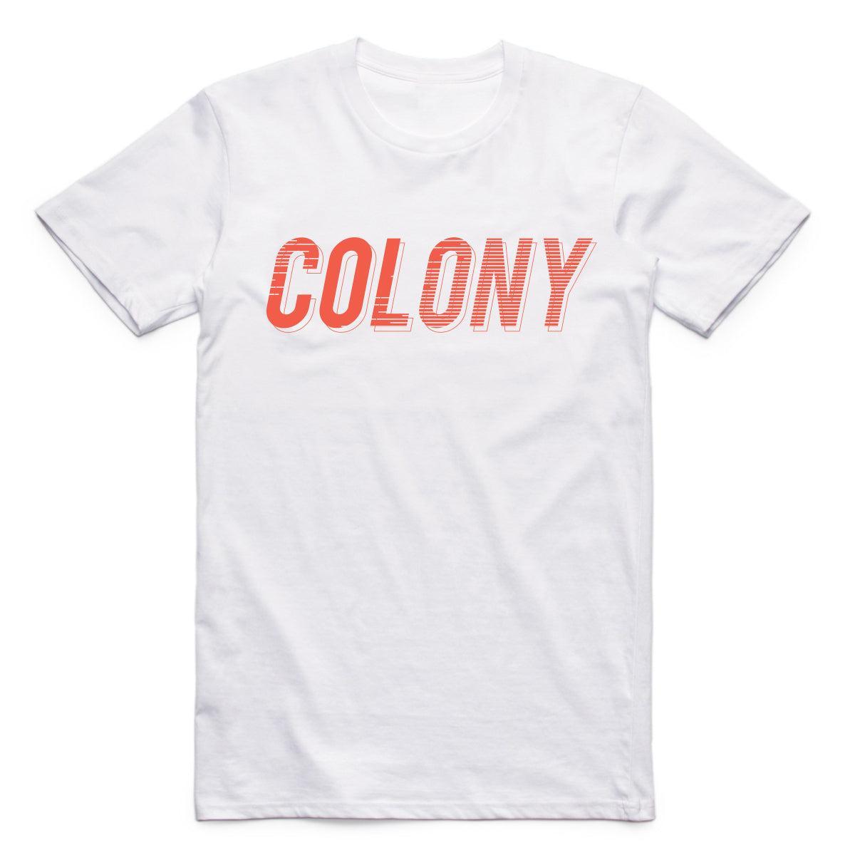 The Colony Momentum T-Shirt is a plain white tee made from 100% carded cotton, featuring "COLONY" in bold orange uppercase letters across the chest.