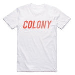 The Colony Momentum T-Shirt is a plain white tee made from 100% carded cotton, featuring "COLONY" in bold orange uppercase letters across the chest.