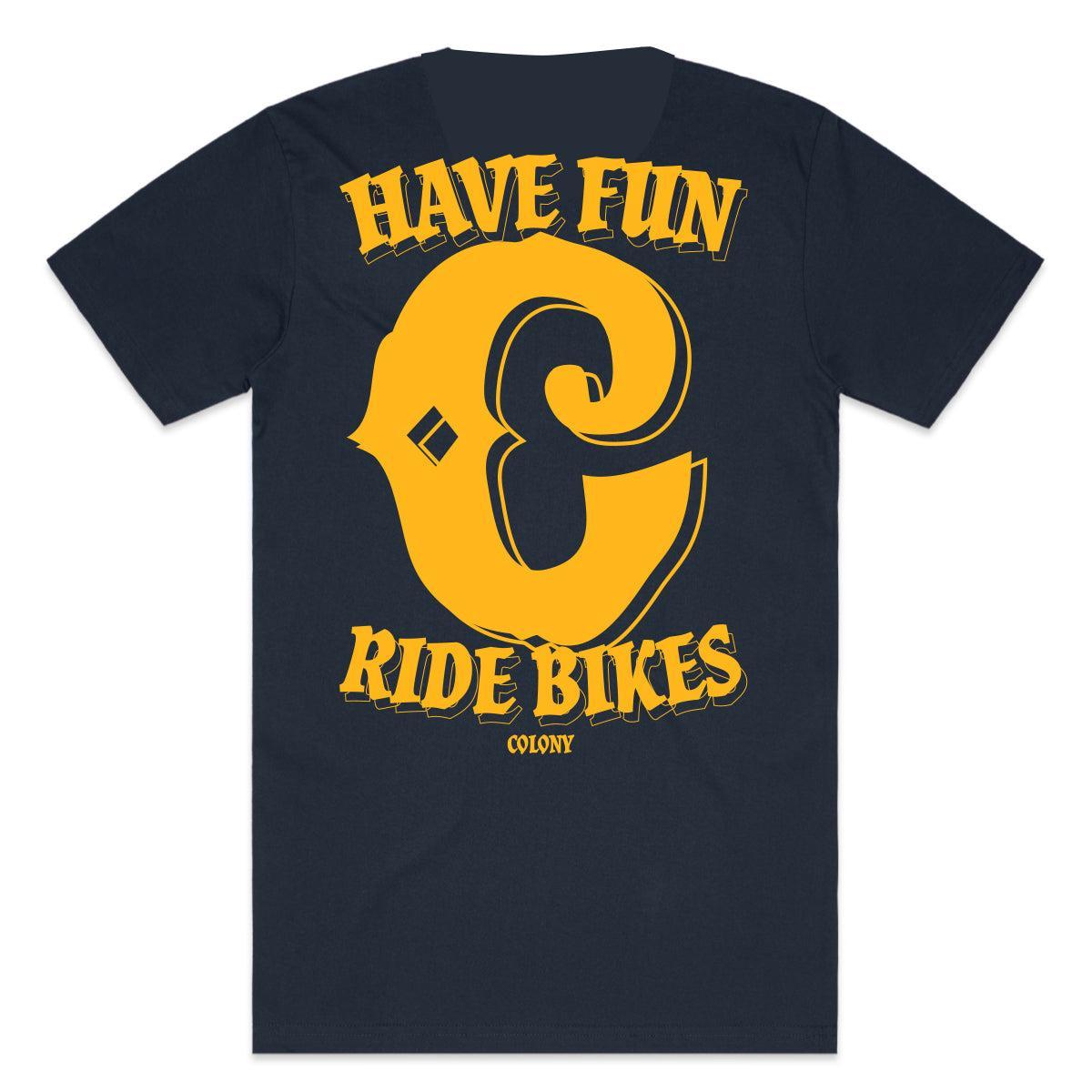 The Colony Have Fun T-Shirt is a navy blue tee made from 100% carded cotton, featuring bold yellow "Have Fun Ride Bikes" text and "Colony" underneath on the back.