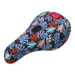 The Odyssey Tropical V1 Pivotal Seat features sublimated artwork with blue, orange, and white tropical leaves on a black background, creating vibrant tropical vibes. It also includes a small red tag attached to the top.