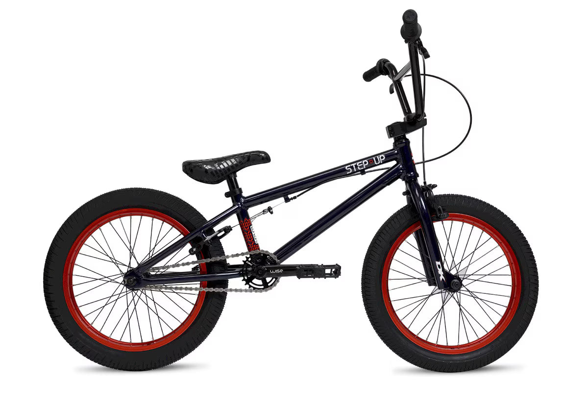 The DK Step Up 18 Inch Bike, shown from the side against a white background, features a black lightweight 6061 aluminum frame, red-rimmed wheels, padded seat, straight handlebars, and visible pedals.