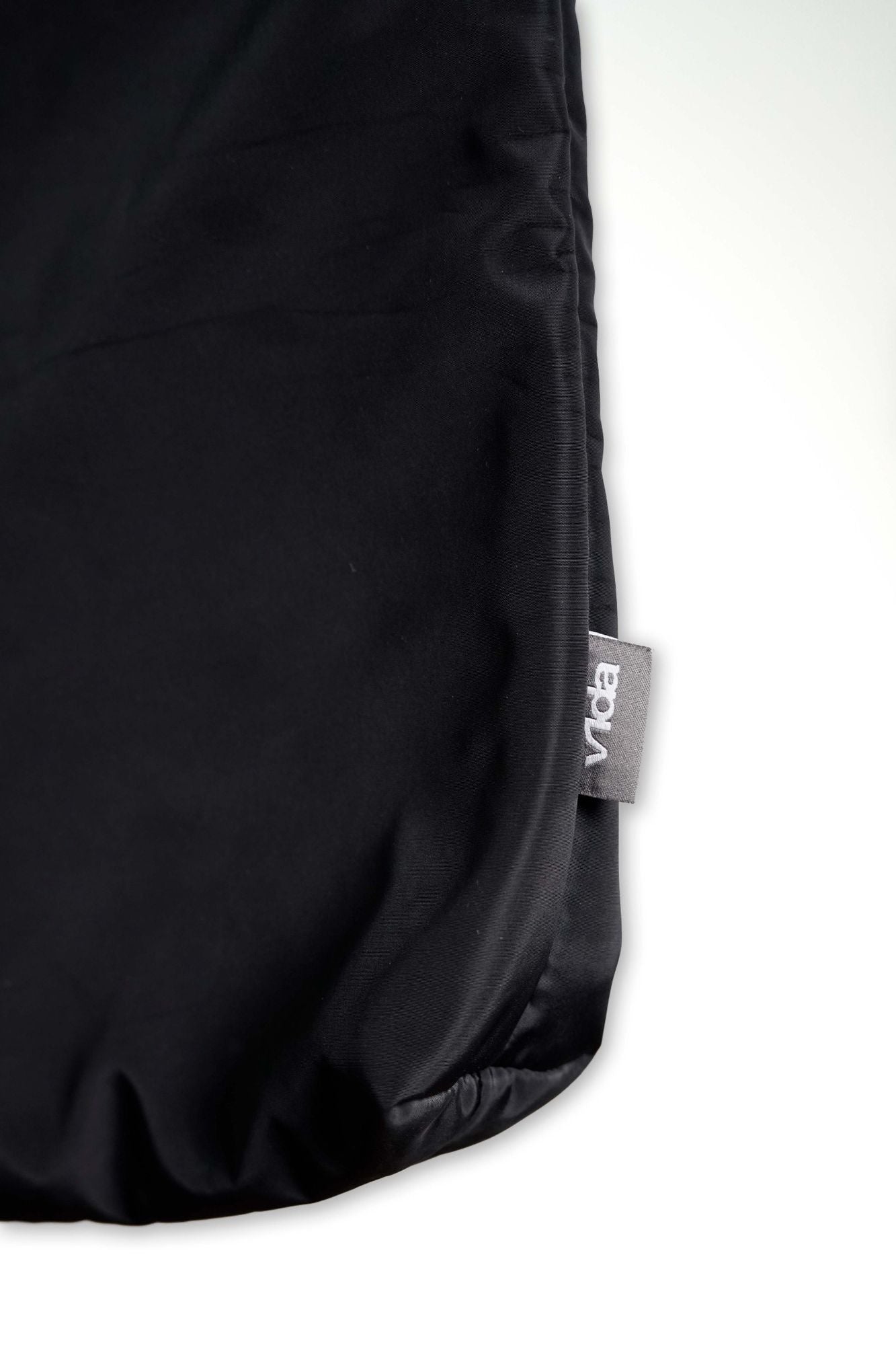 A close-up of the V1da Everything Messenger Bag, a black minimalist design with a small gray "Voda" tag on the edge, displayed against a white background.