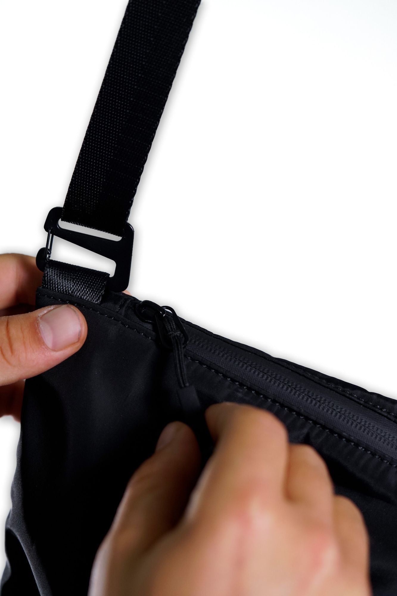 Close-up of hands adjusting a black strap and unzipping a black zipper on the V1da Everything Messenger Bag against a white background.