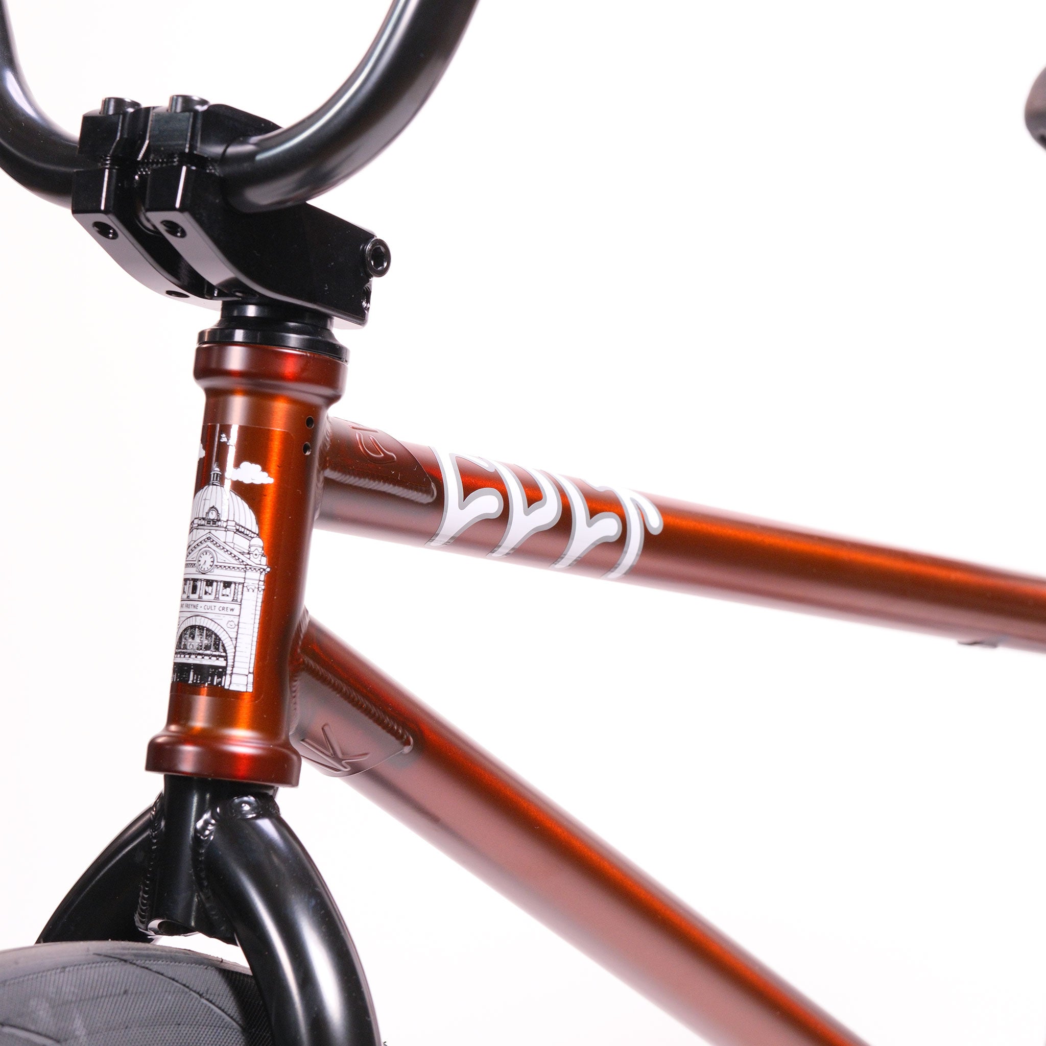 Close-up of a metallic orange Cult Dak X Eclat Custom 'Pat Freyne Signature' BMX frame with white graphics, featuring part of the handlebars, front wheel, and head tube set against a plain white background.