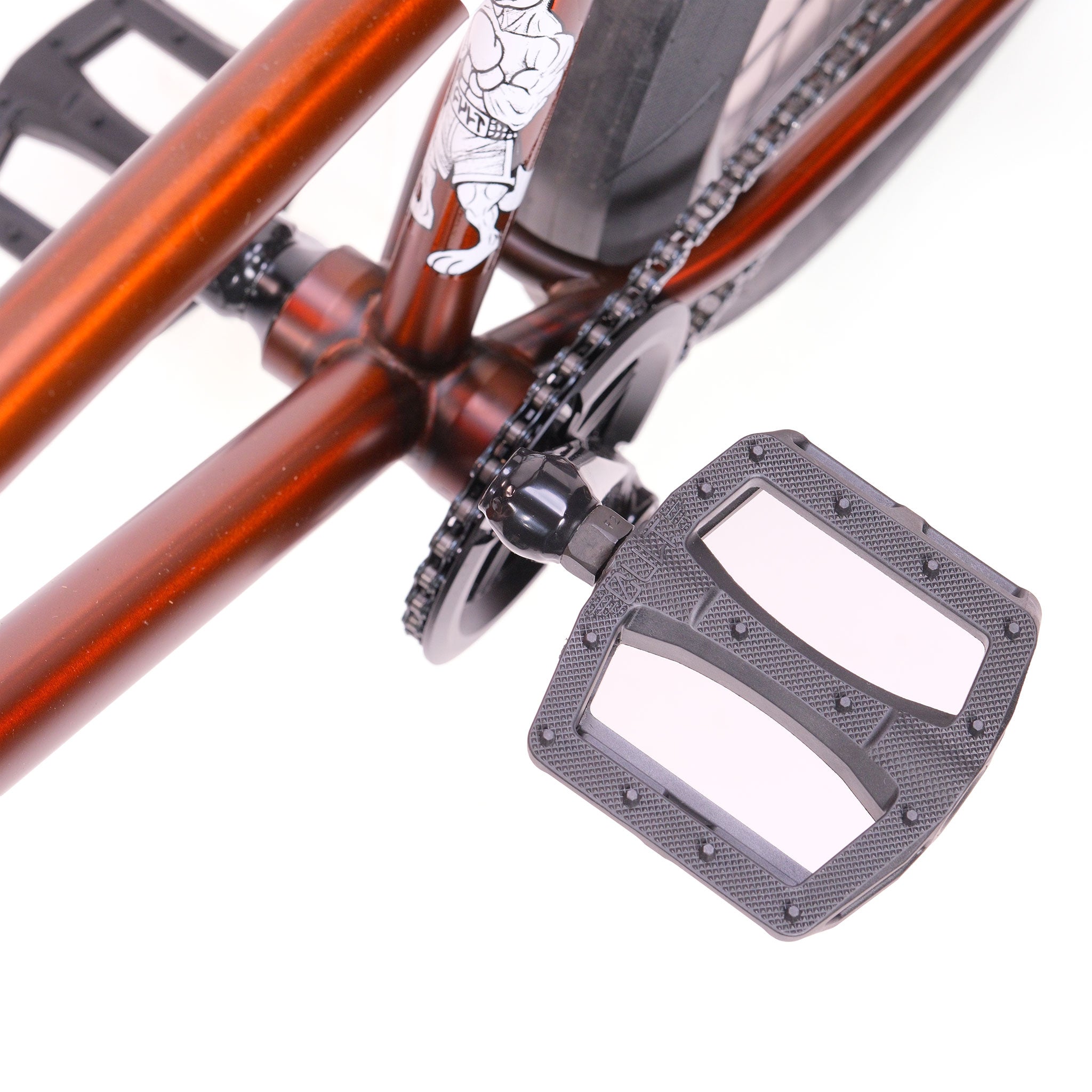 Close-up of a black pedal on the crank arm of an orange Cult Dak X Eclat Custom 'Pat Freyne Signature' BMX bike, showing part of the rear wheel and chain.