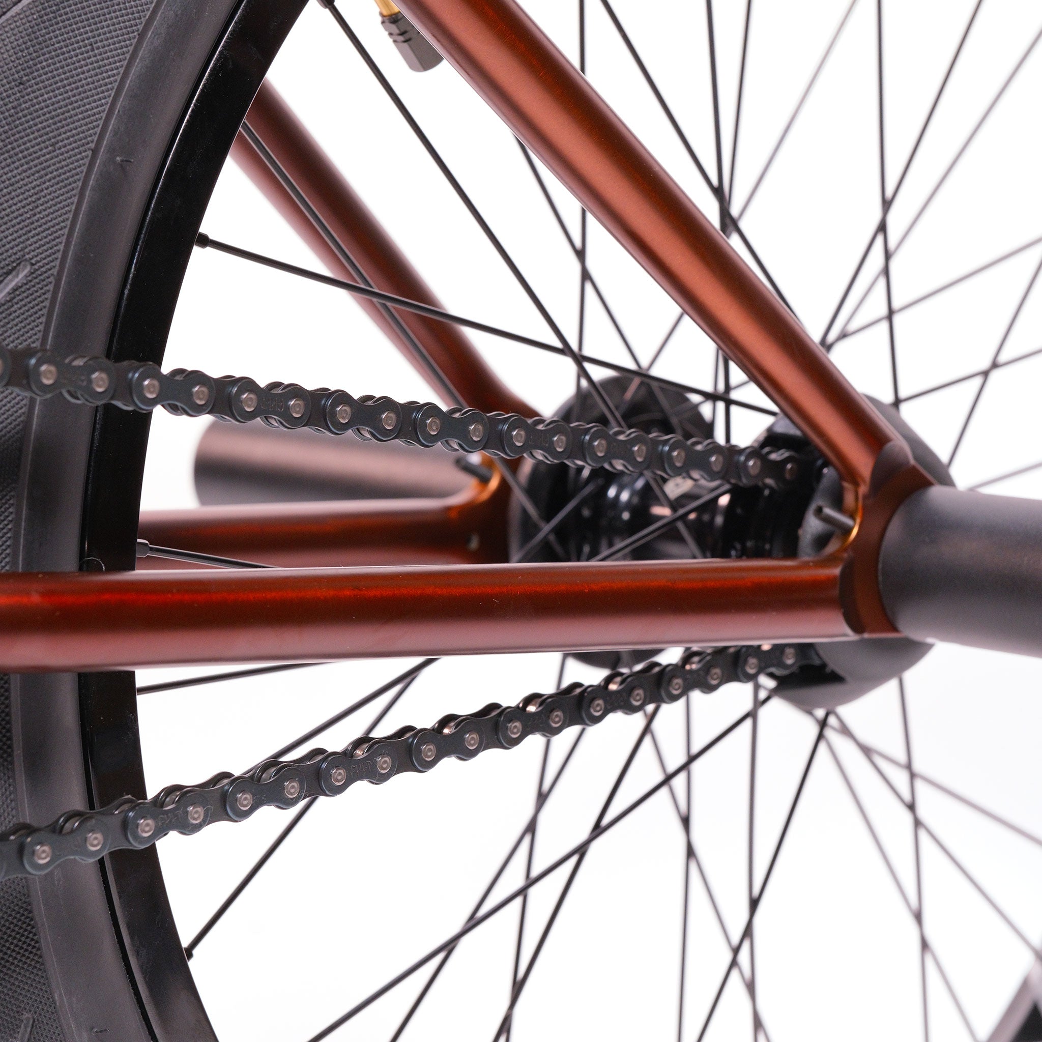 Close-up view of the rear wheel of the Cult Dak X Eclat Custom 'Pat Freyne Signature' BMX bike, showing spokes, tire, and chain with a reddish-brown frame against a white background.