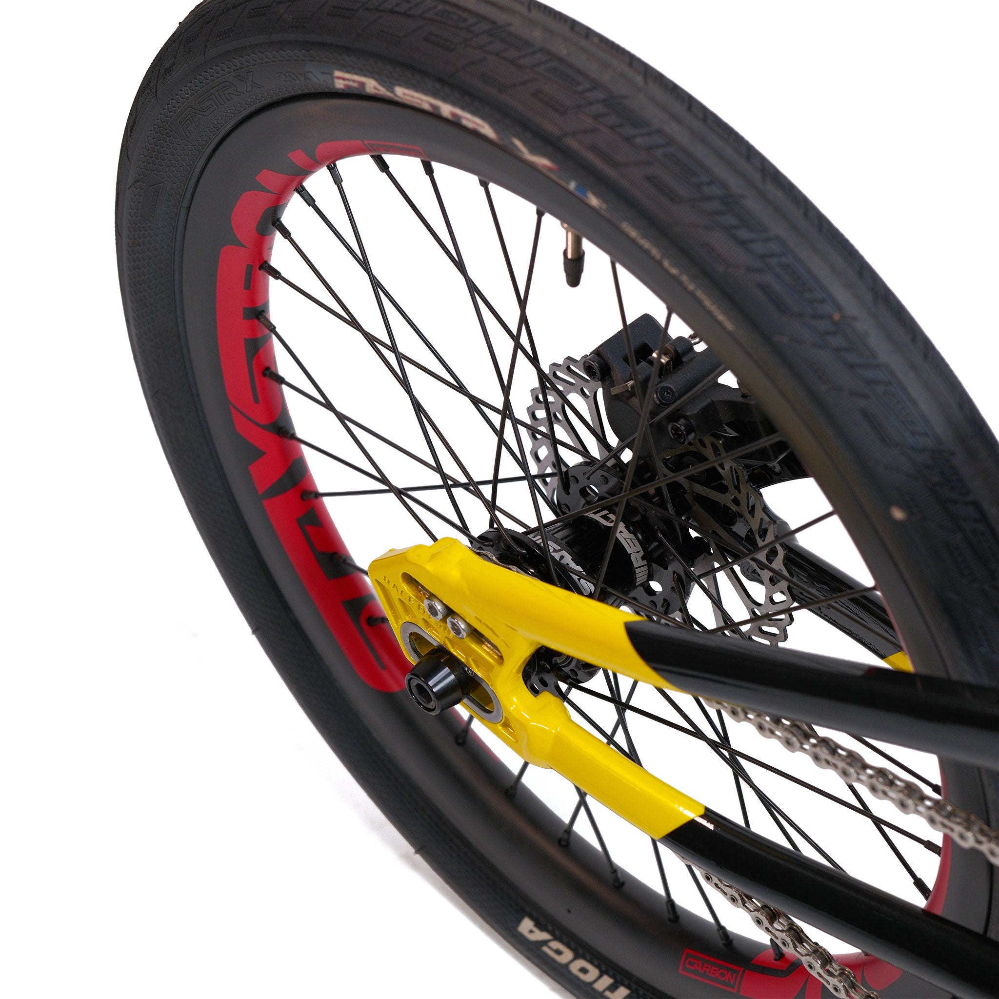 Close-up of the Stay Strong V5.1 Pro XXXL Race Bike’s rear wheel, featuring a black tire, red label, yellow axle mount, disc brake, and visible chain—highlighting the precision engineering and lightweight aluminium frame that define this custom race bike.
