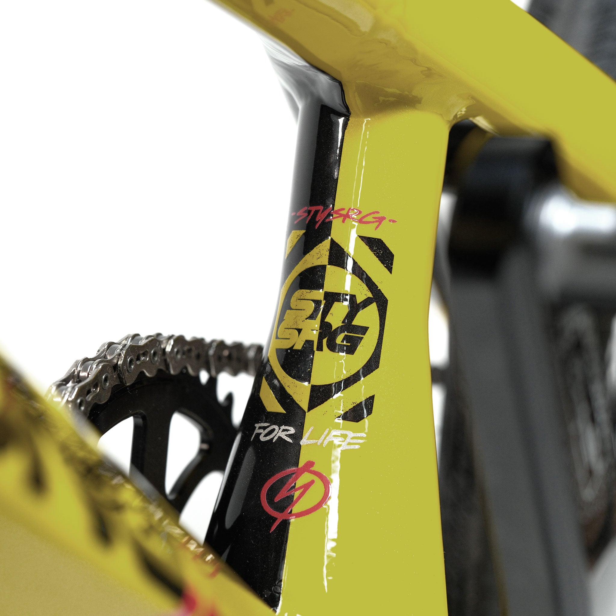 Close-up of a yellow and black Stay Strong V5.1 Pro XXXL Race Bike frame, featuring the logo "STY SA6," the phrase "FOR LIFE," and gear components in the background—highlighting the precision engineering of this custom race bike’s high-performance aluminium frame.