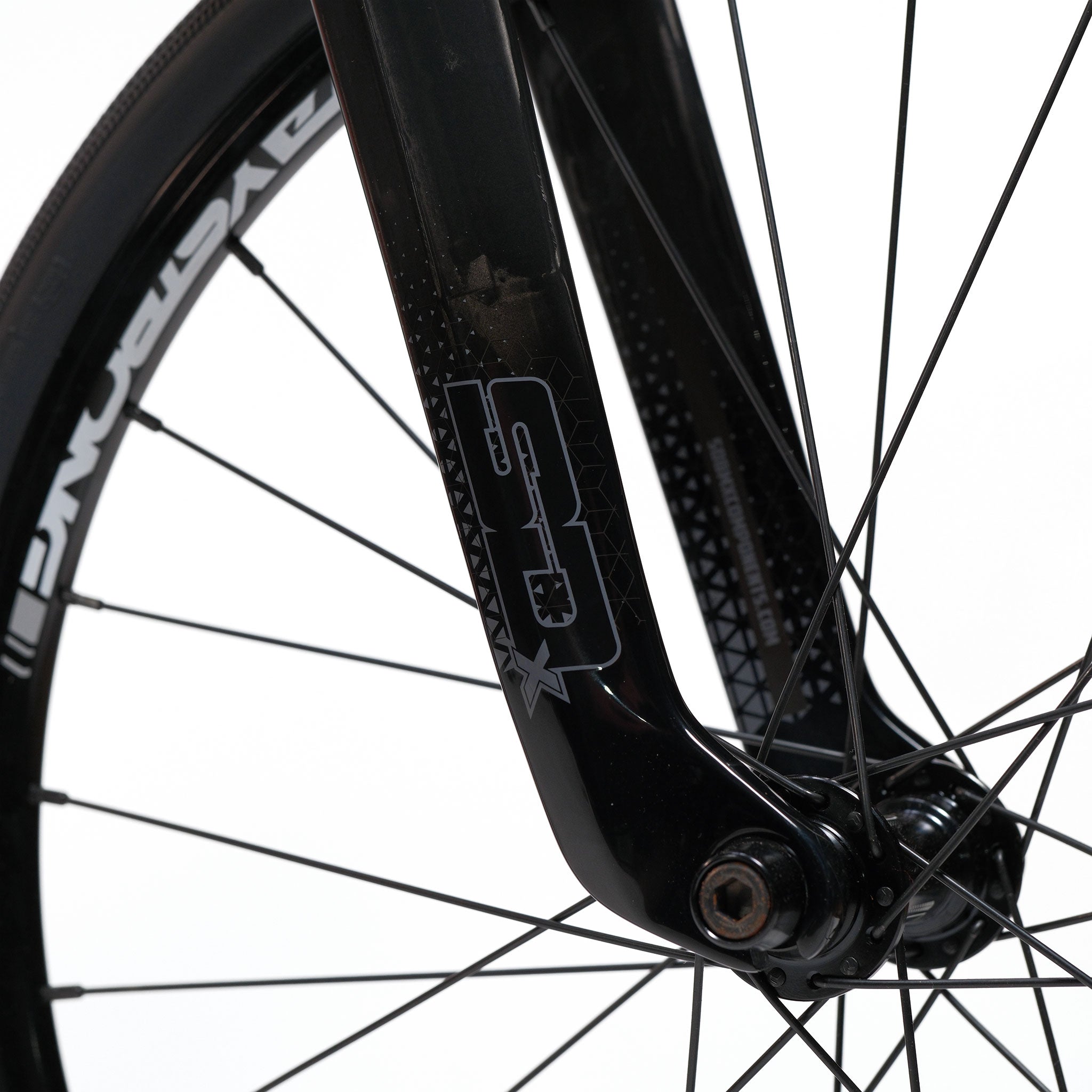 Close-up of the Stay Strong V5.1 Junior Race Bike's black front fork with "S2X" logo, highlighting the spokes and a section of a CYCLOPRANE tire against a white background. The lightweight aluminium construction reflects its purpose-built design for speed and agility in BMX racing.
