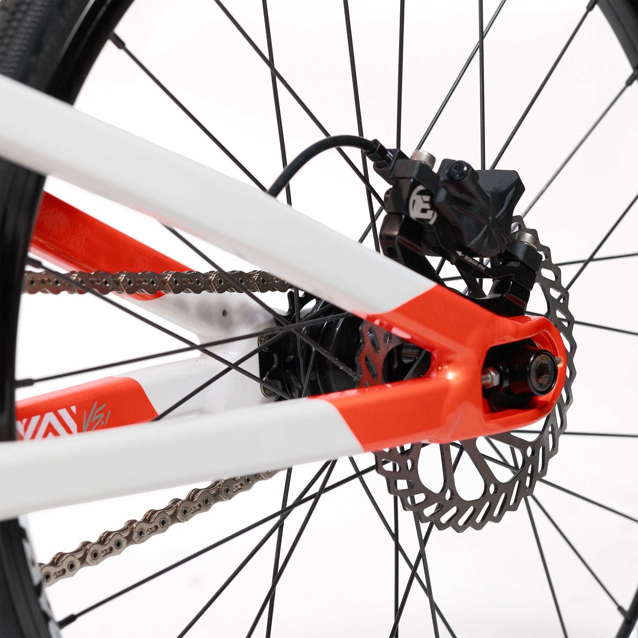 Close-up of the Stay Strong V5.1 Junior Race Bike’s rear wheel featuring the disc brake, black caliper, chain, and part of its red and white aluminium frame.