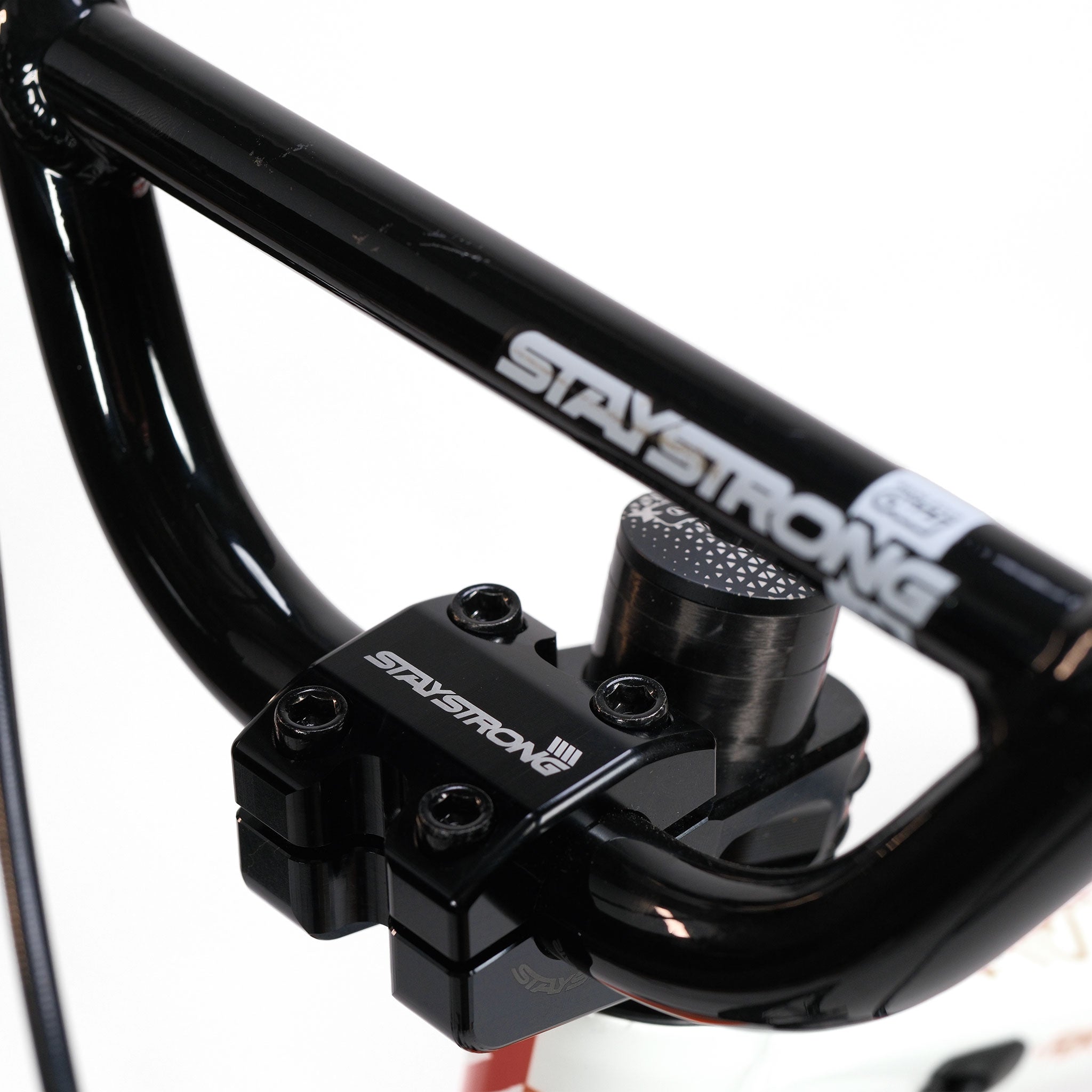 Close-up of a black handlebar and stem with bold white "STAY STRONG" branding, crafted from lightweight aluminium, featured on the Stay Strong V5.1 Junior Race Bike against a plain white background. Perfect for upgrading any BMX race bike or junior disc frame.