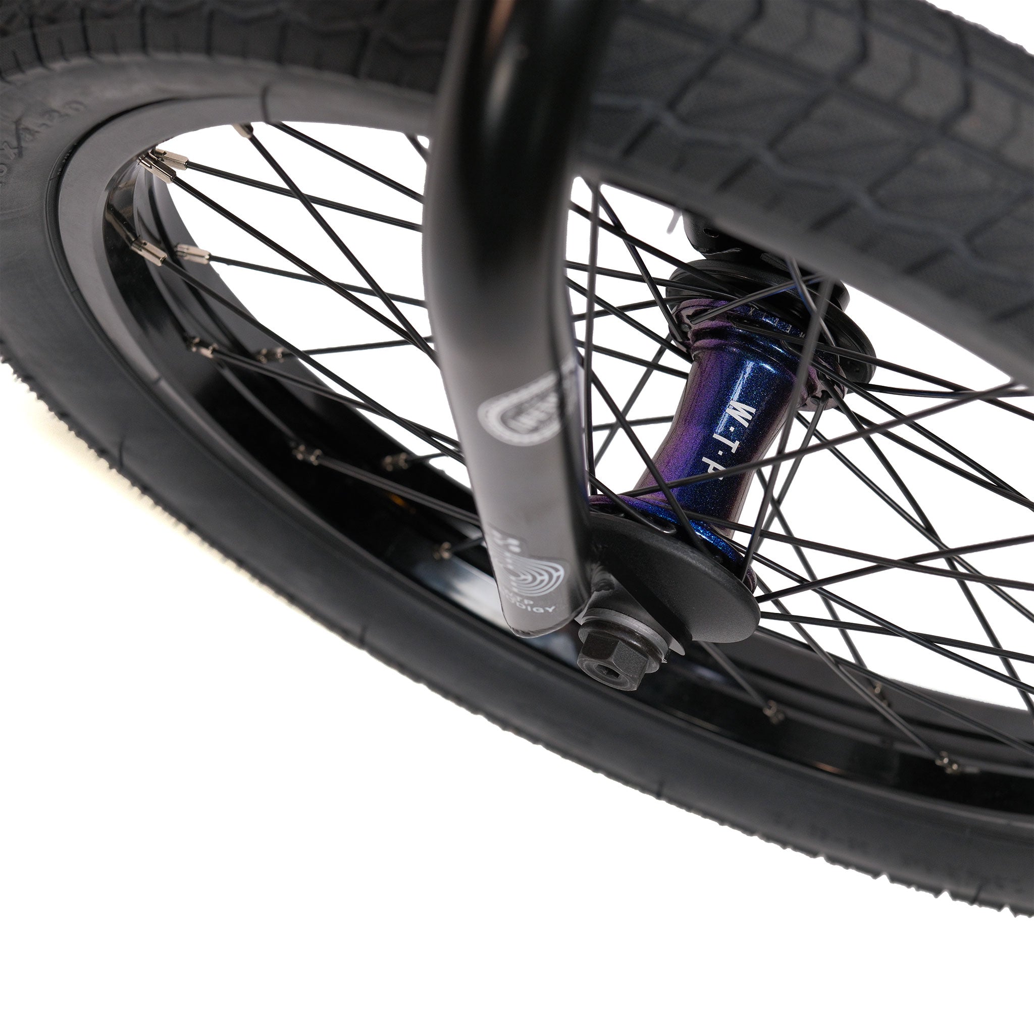 Close-up of a BMX bike wheel with black spokes, a purple metallic hub, and a black tire, set against a white background. This detailed shot highlights the premium Éclat components featured on the Wethepeople Prodi-G-Unit 18 Inch Custom Bike.