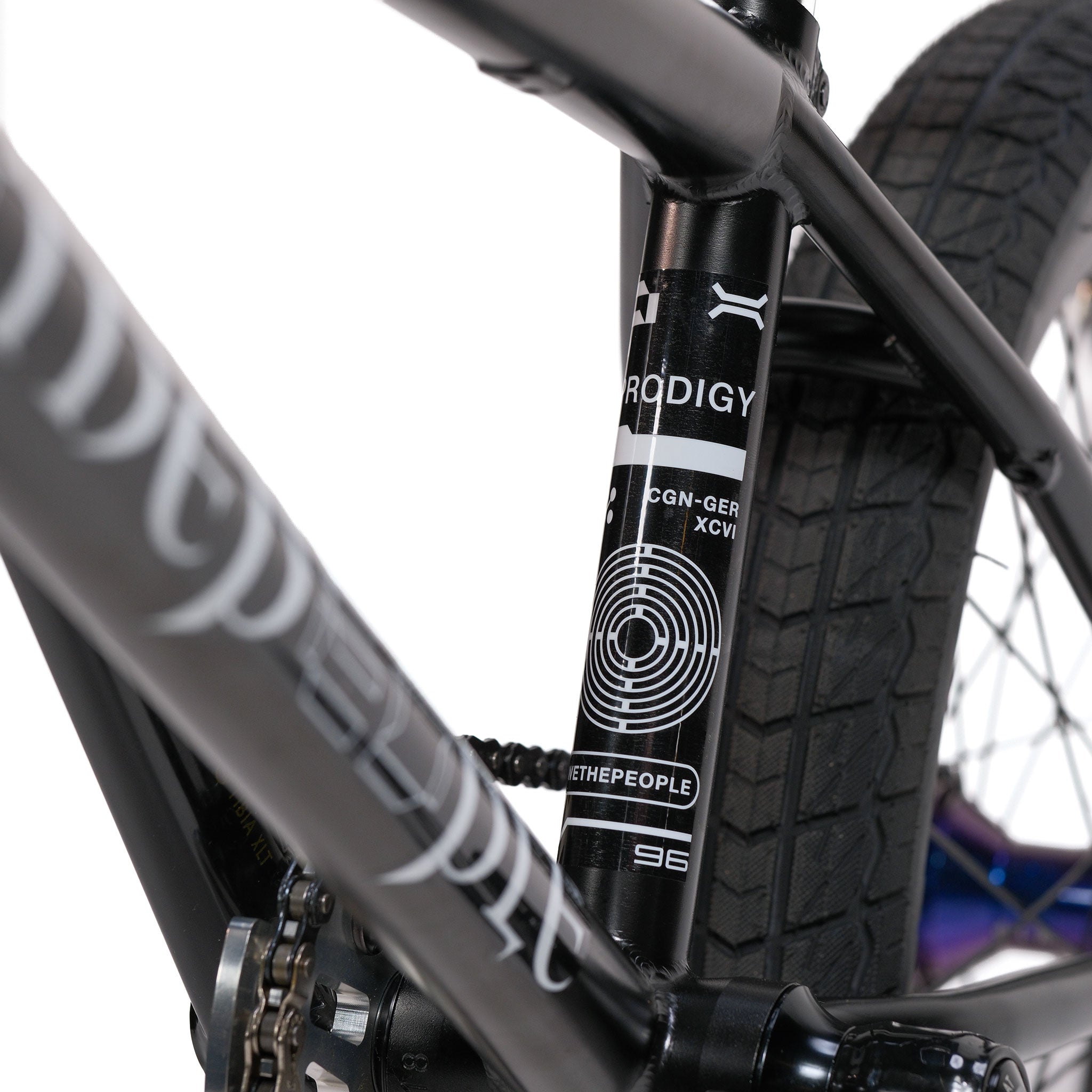 Close-up of the Wethepeople Prodi-G-Unit 18 Inch Custom Bike’s black frame, highlighting brand logos, a circular design element, and a section of the rear tire against a white background. This BMX bike is equipped with premium Eclat components and features distinctive Wethepeople Prodi-G-Unit detailing for a professional finish.