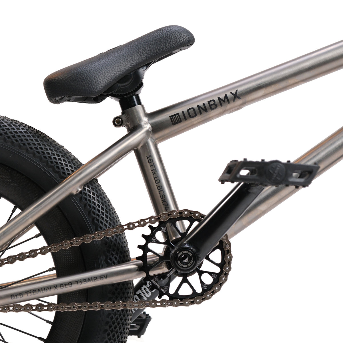 Close-up of the ION BMX Ti16 Custom Titanium 16 Inch Bike, highlighting its seat, rear wheel, pedals, crank, and chain. The lightweight silver titanium frame features visible “ION BMX Ti16” branding.
