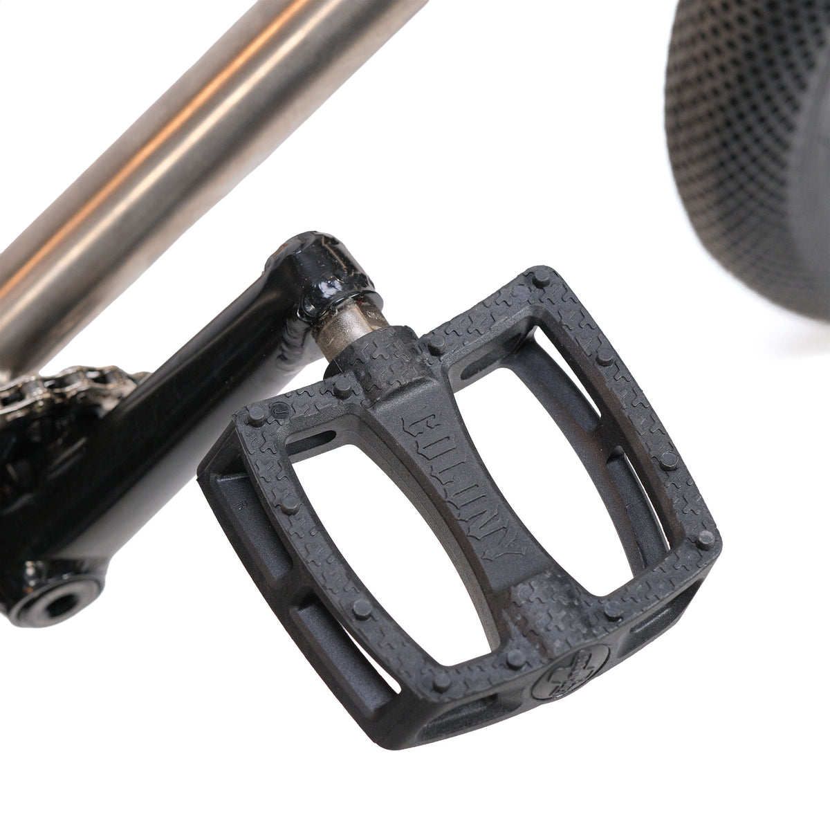 Close-up of a black BMX bicycle pedal attached to a crank arm, with part of the rear tire visible in the background—perfect for the ION BMX Ti16 Custom Titanium 16 Inch Bike or other lightweight BMX setups.