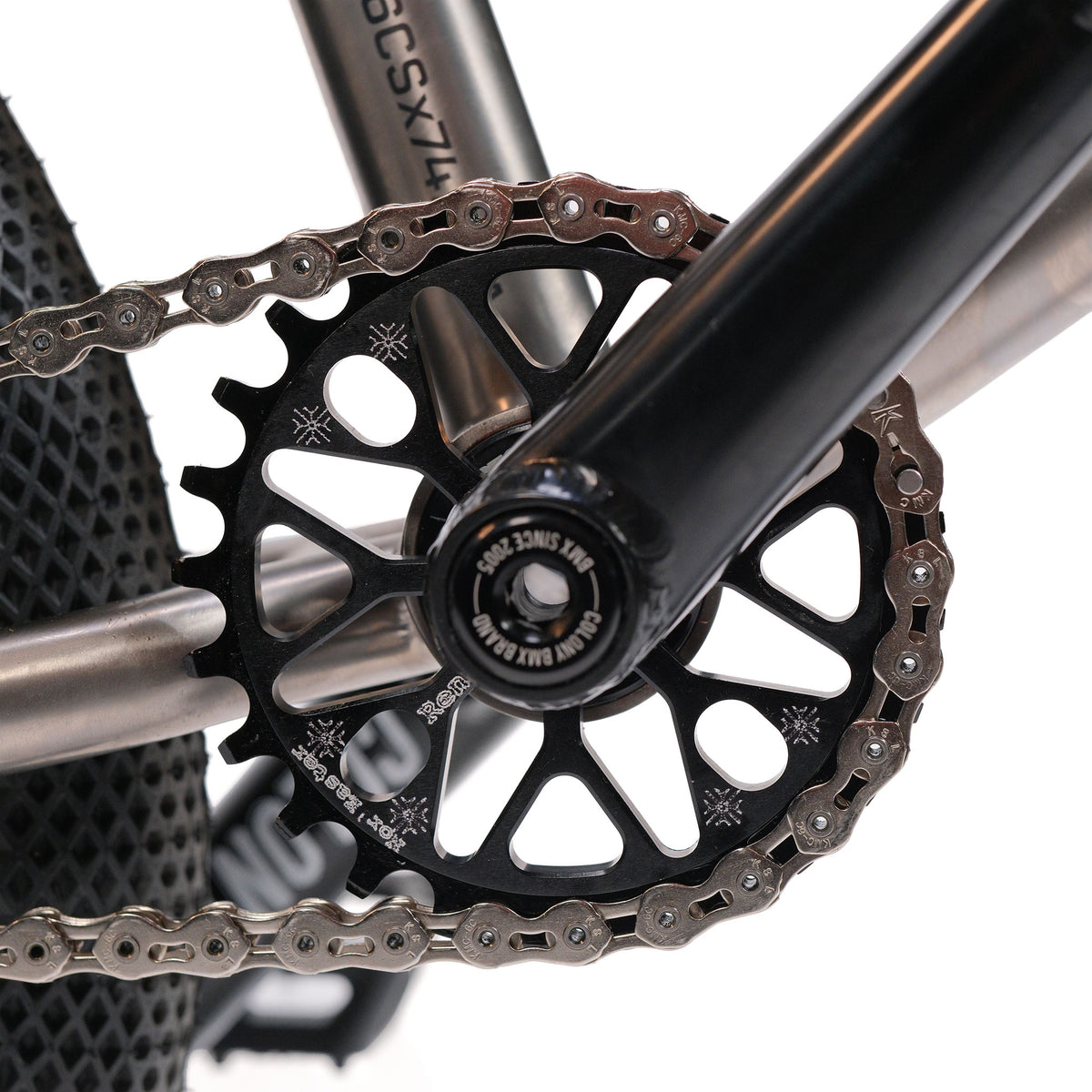 Close-up of the crankset on the ION BMX Ti16 Custom Titanium 16 Inch Bike, highlighting the chainring, chain, and part of the lightweight titanium frame with a textured rear tire in the background.
