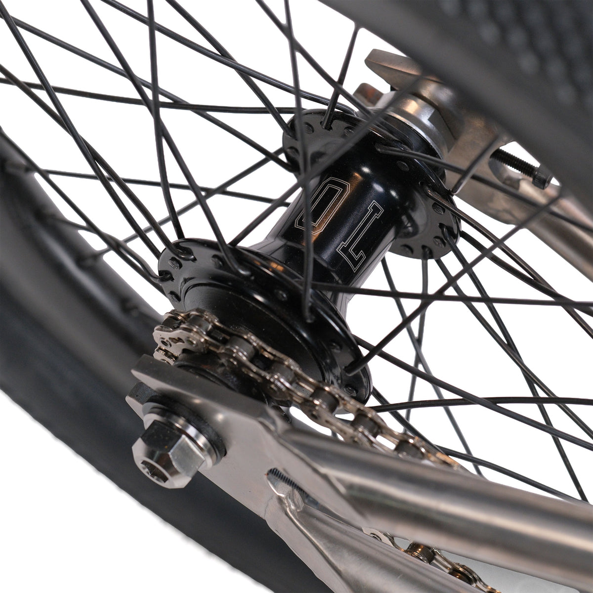 Close-up of the ION BMX Ti16 Custom Titanium 16 Inch Bike’s rear wheel, highlighting the hub, spokes, chain, and sections of the tire and frame, with the metal axle bolt and chain tensioner clearly visible.