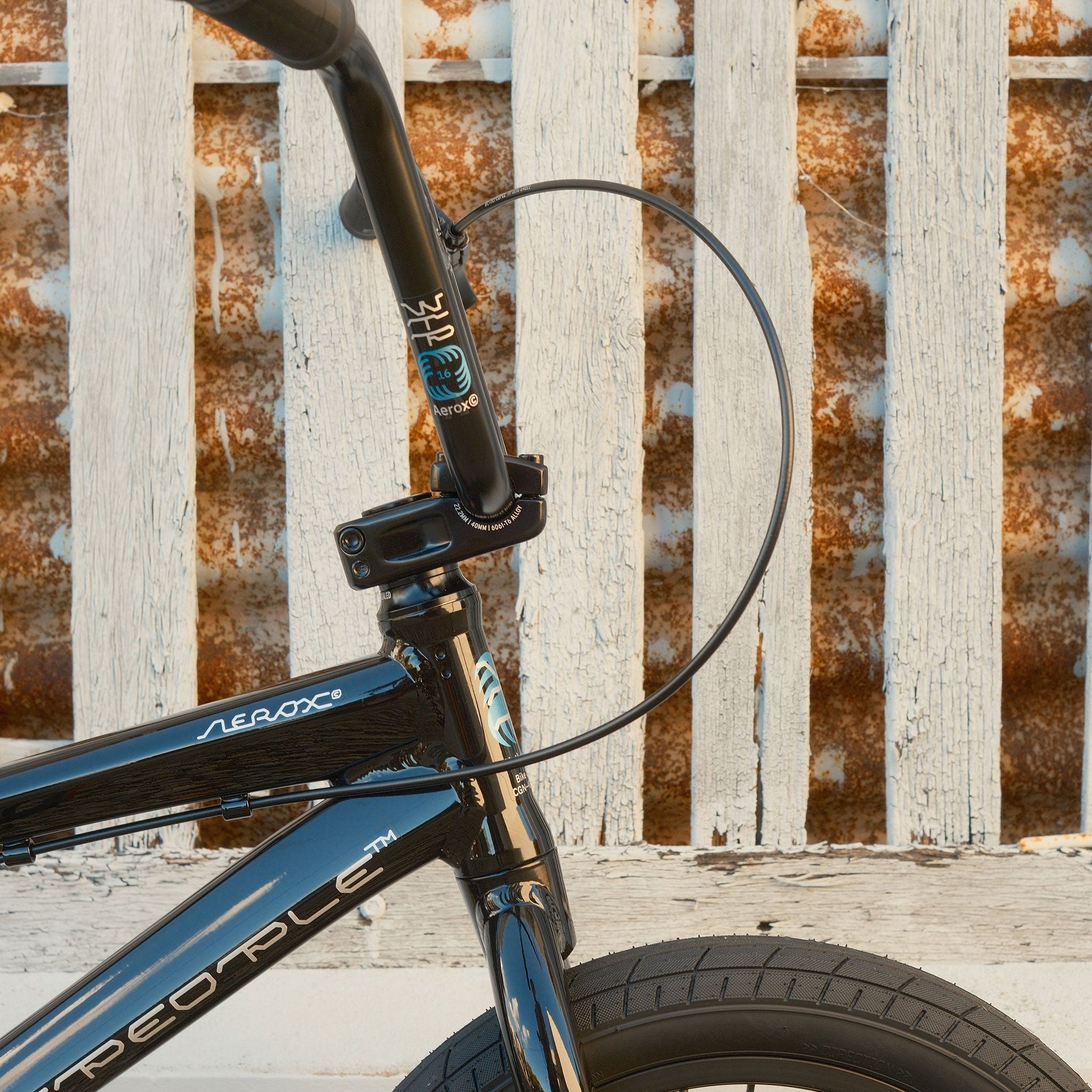 Close-up of the Wethepeople Aerox 16 Inch Bike’s handlebars and front wheel, showcasing its lightweight alloy frame, set against a weathered white wooden fence with rust stains.