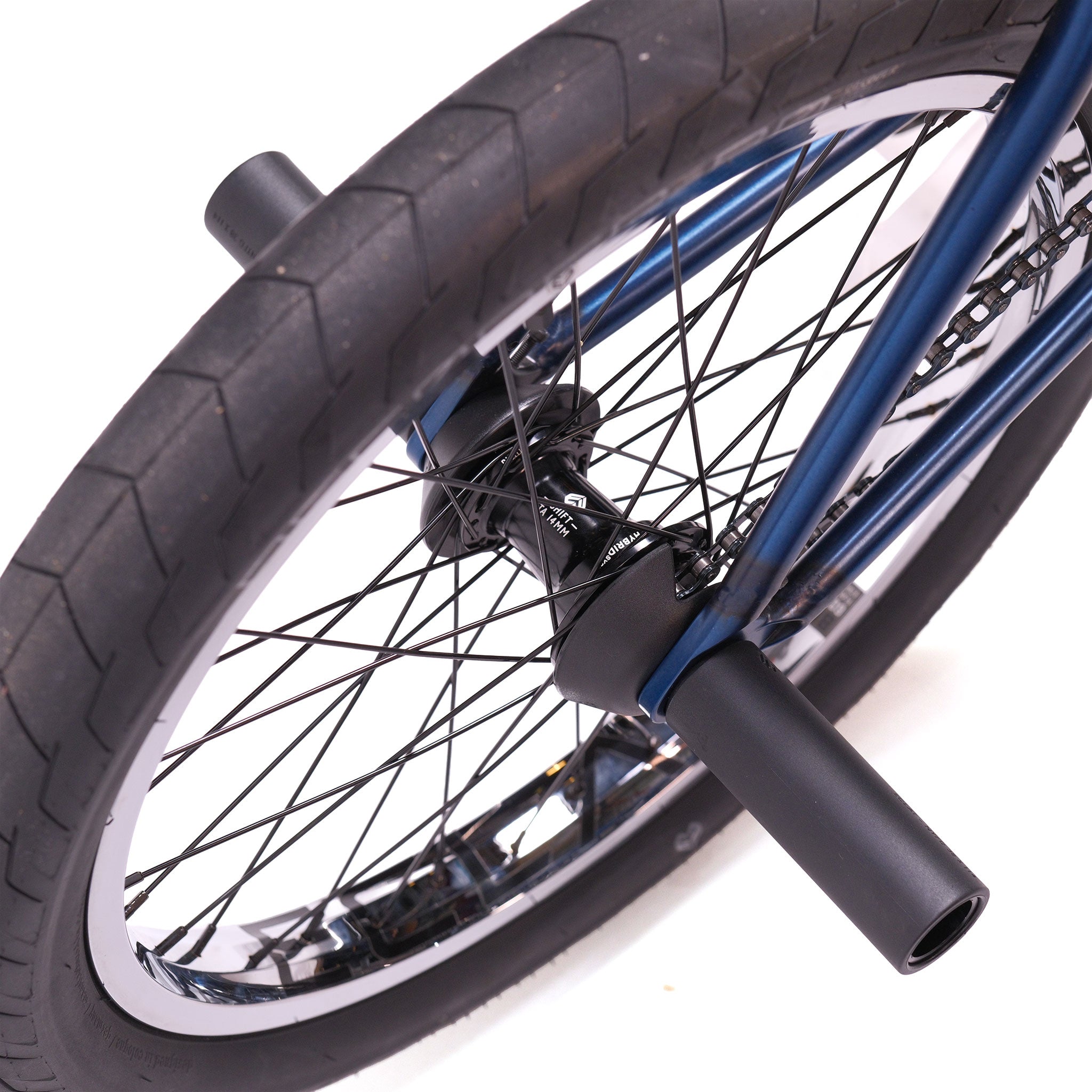 Close-up of a custom BMX bike’s rear wheel with black pegs on the axle, highlighting tire tread, spokes, and part of the blue Wethepeople Tomorrow X TA Custom build frame.
