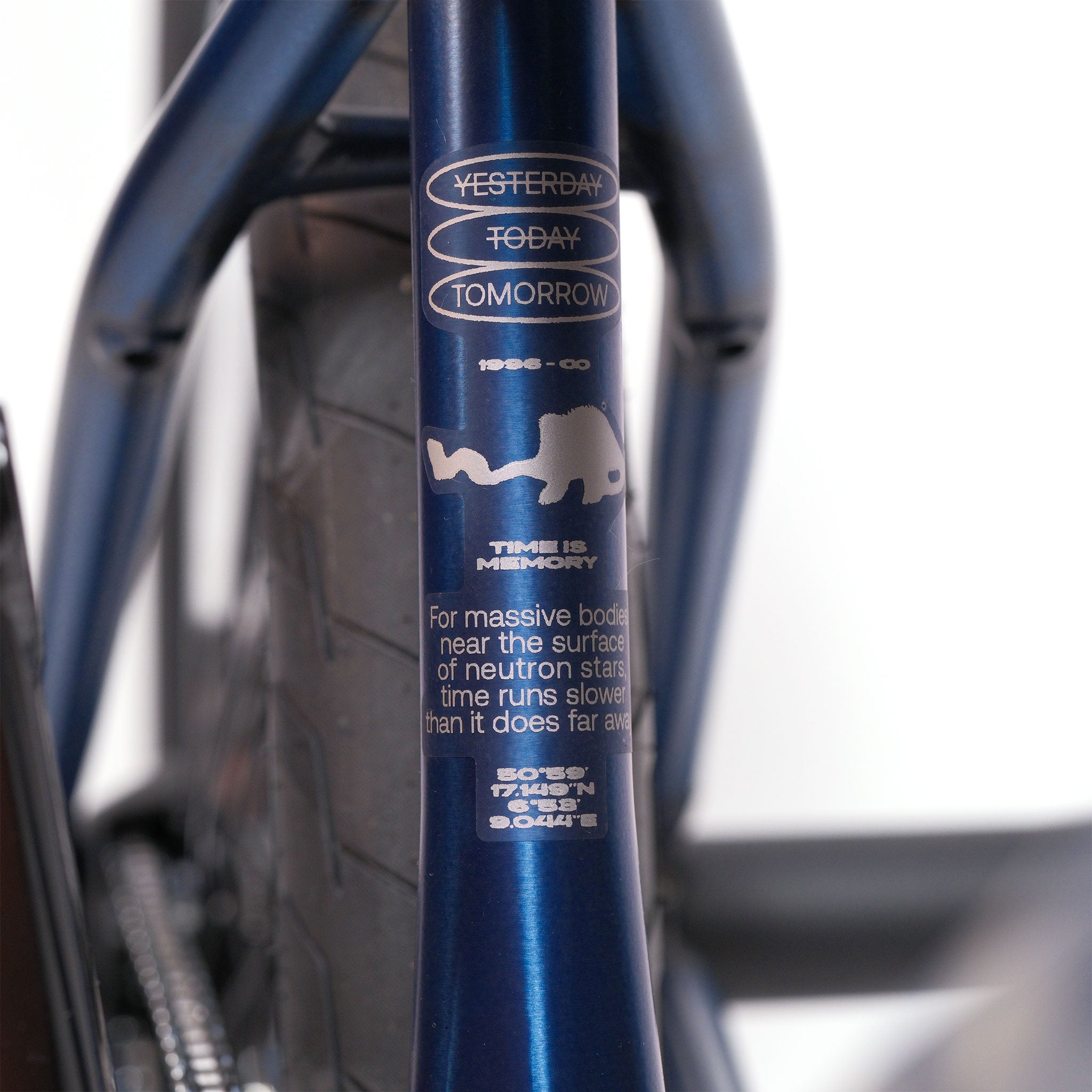 Close-up of a Wethepeople Tomorrow X TA Custom build frame behind a rear tire, featuring graphics and text about time relativity near neutron stars on this unique BMX bike.