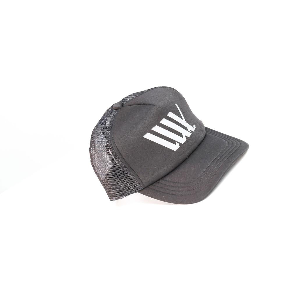 The LUXBMX Flag Trucker Cap features a black mesh back, solid front with white "LWK" lettering, and is made in Brisbane from recycled polyester. Shown on a plain white background.