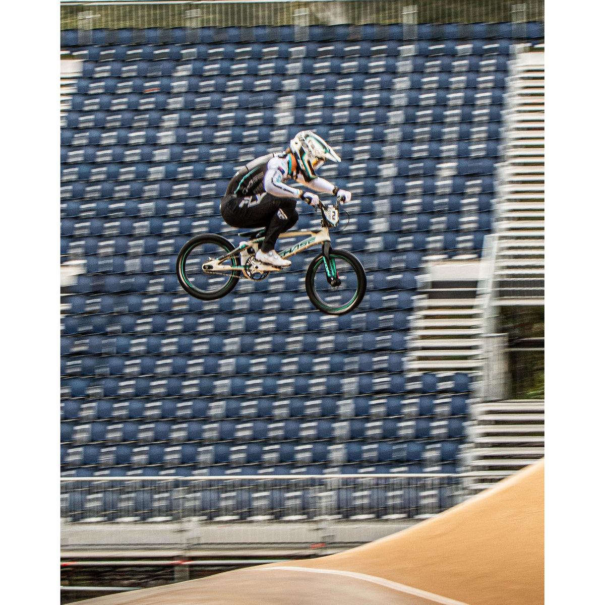 Capture the excitement of the NSW State Championships with the LUXBMX NSW State Championship’s 2026 Photo Packages – Lake Mac: a BMX rider soaring mid-air above a dirt track, empty blue and white stadium seats framing the background—a dynamic shot ideal for racers and fans seeking memorable event photography.